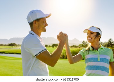 Shot of male and female friends giving high-five at golf course. Professional golfers shaking hands after the game.