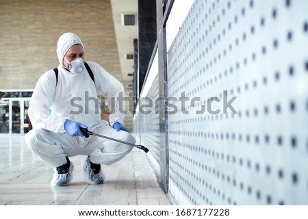 Shot of male person in white chemical protection suit doing disinfection of public areas to stop spreading highly contagious corona virus. Stop coronavirus or COVID-19.