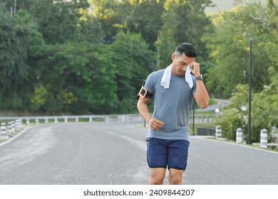 Shot of man runner wiping sweat with a towel while running in the city park - Powered by Shutterstock