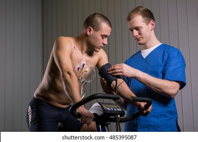 Shot of a man sitting on a stationary bike and looking at his arm while medic is checking his blood pressure