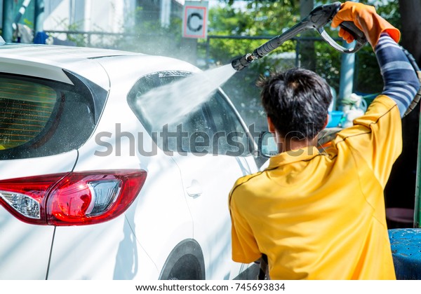 Shot of a man washing his car under high\
pressure water outdoors. Cleaning Car Using  high pressure water\
jet. Washing with soap. a worker apply water jet to a Car for his\
car care business.