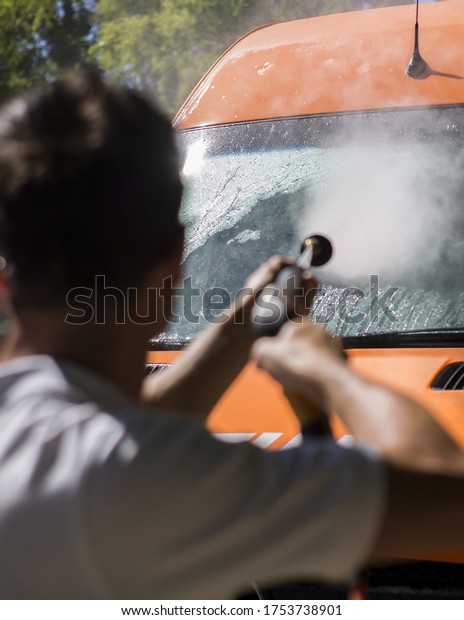 A shot of a man washing an orange car with a car\
washing spray