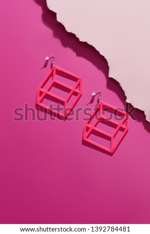A shot of massive hotpink dangle earrings with volume effect. The voguish set is isolated asymmetrically against the pink background, near pale pink ragged platform. Fashionable women's fashion item.