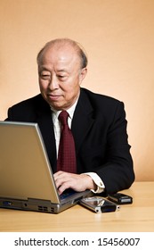 A Shot Of A Mature Asian Businessman Working On His Laptop