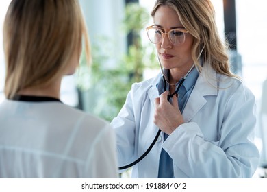 Shot Of Mature Confident Female Doctor Examining With Stethoscope To Young Patient In The Medical Consultation.