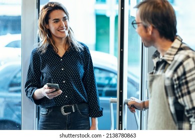 Shot Of Mature Dependent Greeting A Smiling Woman Entering An Organic Grocery Store.