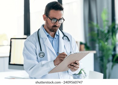 Shot of mature male doctor with stethoscope over neck taking notes in clipboard in a medical consultation - Powered by Shutterstock