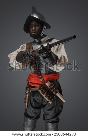 Shot of medieval soldier dressed in steel armor and helmet aiming flintlock musket.