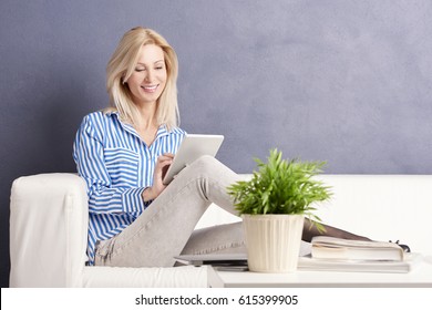 Shot Of A Mid Age Woman Working Online On Digital Tablet While Sitting On Couch At Home.