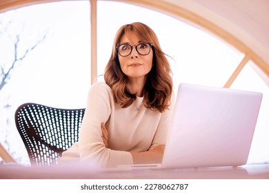 Shot of a mid aged businesswoman sitting at desk in the office with laptop and looking thoughtfully. - Powered by Shutterstock