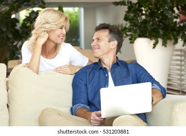 Shot Of A Middle Aged Couple Using Laptop While Sitting On Sofa At Home.