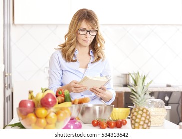 Shot of a middle aged woman reading her recipe book while cooking at home.