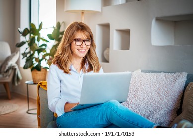 Shot of a middle aged woman using a laptop on the sofa at home. Businesswoman working from home.