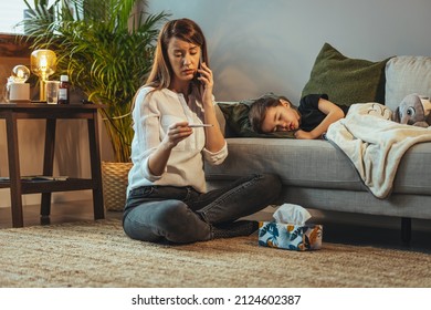 Shot Of A Mother Making A Phone Call While Aiding To Her Sick Young Son At Home. Mother Checking Temperature Of Her Sick Son. Close Up Of A Mother Checking The Temperature Of Her Boy 