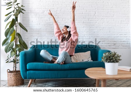 Shot of motivated young woman listening to music with digital tablet while sitting on sofa at home.