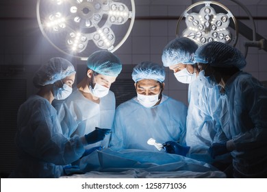 Shot of a multiracial surgeon team consists of trained surgeons, trauma specialists and plastic surgeons, consulting during difficult operation proceed, standing before unconscious patient in O.R. - Shutterstock ID 1258771036