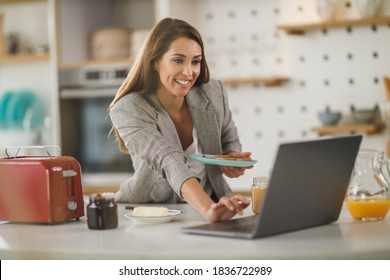 Shot Of A Multi-tasking Young Business Woman Surfing On Social Media And Having A Breakfast At Home While Getting Ready To Go To Work.