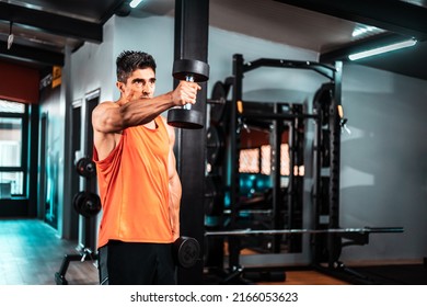 Shot Of A Muscular Guy In Sportswear Working Out With Dumbbells At The Cross Training Gym. He Is Pumping Up Shoulders Muscule With Heavy Weight.
