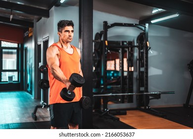 Shot Of A Muscular Guy In Sportswear Working Out With Dumbbells At The Cross Training Gym. He Is Pumping Up Shoulders Muscule With Heavy Weight.
