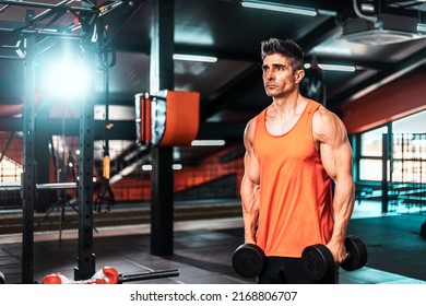 Shot Of A Muscular Guy In Sportswear Working Out With Dumbbells At The Cross Training Gym. He Is Pumping Up Shoulders Muscule With Heavy Weight.
