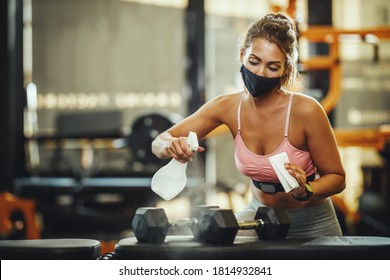 Shot Of A Muscular Young Woman With Protective Mask Cleaning Fitness Gym Equipment Afther Workout During Covid-19 Pandemic.