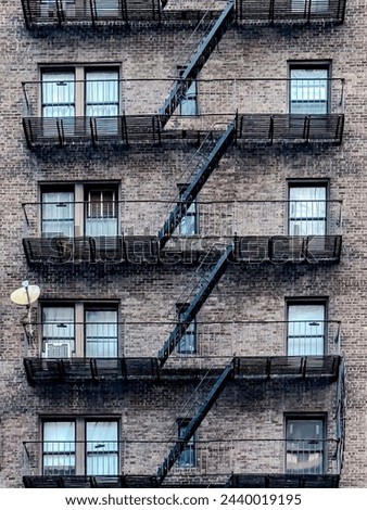 A shot of an old brick building with balconies and the fire escape painted black. Taken on a sunny morning in New York City.