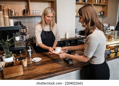 Shot Of Old Woman Coffee Maker Serving Her Customer In Coffee Bar.