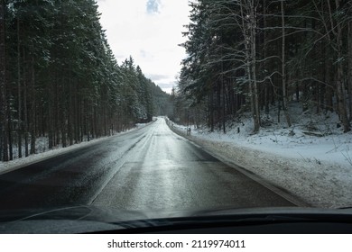 A Shot On The Move From Behind The Windshield Of An Electric Car With Snow-covered Mountains. Cold Cloudy Winter Day. POV First Person View Shot On A Asphalted Mountain Road. Selective Focus.