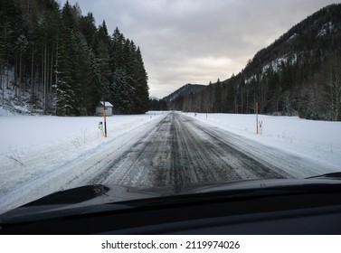 A Shot On The Move From Behind The Windshield Of An Electric Car With Snow-covered Mountains. Cold Cloudy Winter Day. POV First Person View Shot On A Snowed Mountain Road. Selective Focus.