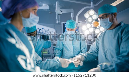 Shot in the Operating Room Assistant Hands out Instruments to Surgeons During Operation. Surgery in Progress. Professional Medical Doctors Performing Surgery.