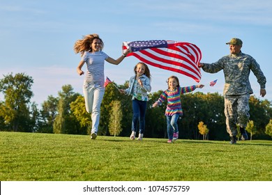 Shot Of Patriotic Family Running With Flag. US Soldier And His Happy Family.