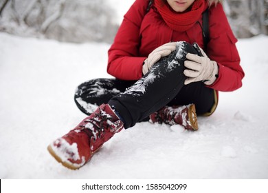 Shot Of Person During Falling In Snowy Winter Park. Woman Slip On The Icy Path, Fell, Injury Knee And Sitting In The Snow. Danger Of Season Trauma.