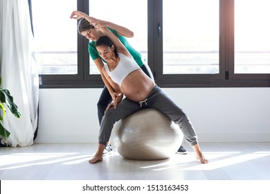 Shot of physiotherapist helping to beautiful pregnant woman for doing pilates exercises with ball preparing for childbirth.