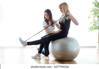Shot of physiotherapist helping patient to do exercise on fitness ball in physio room.