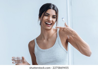 Shot of pretty young woman brushing her teeth while looking at camera in the bathroom at home. - Powered by Shutterstock