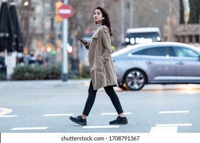 Shot of pretty young woman crossing the street while listen to music with the wireless earphones.