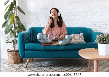 Shot of pretty young woman listening to music with digital tablet and relaxing while sitting on sofa at home.