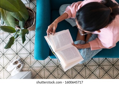 Shot Of Pretty Young Woman Reading A Book While Sitting On Sofa At Home. Top View.