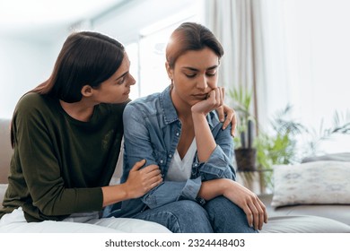 Shot of pretty young woman supporting and comforting her sad friend while sitting on the sofa at home. - Powered by Shutterstock