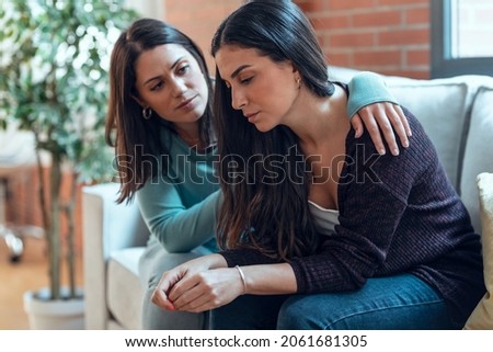 Shot of pretty young woman supporting and comforting her sad friend while sitting on the sofa at home.