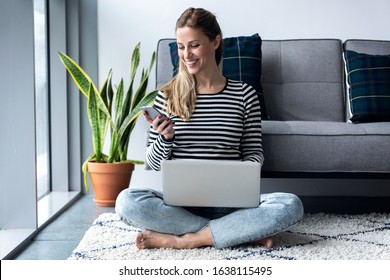 Shot of pretty young woman using her mobile phone while working with laptop sitting on the floor at home. - Shutterstock ID 1638115495