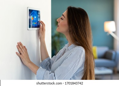 Shot of pretty young woman using the home automation system on digital tablet to regulate the temperature.