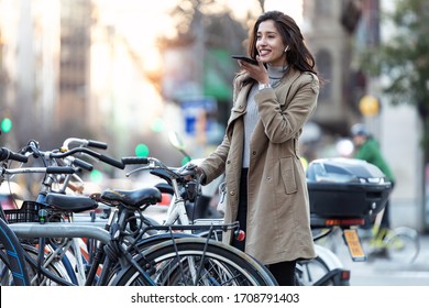 Shot of pretty young woman using voice recognition system on her smartphone while standing in the street.