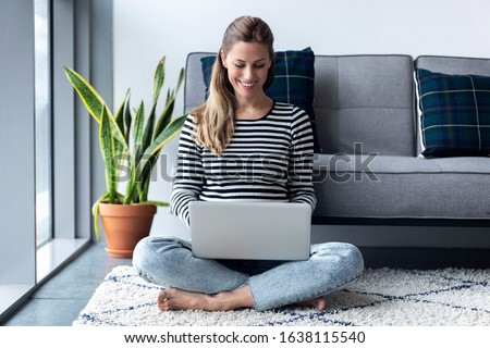 Shot of pretty young woman using her laptop while sitting on the floor at home.