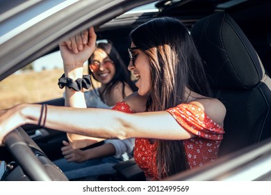 Shot Of Pretty Young Women Singing While Driving A Car On Road Trip On Beautiful Summer Day.