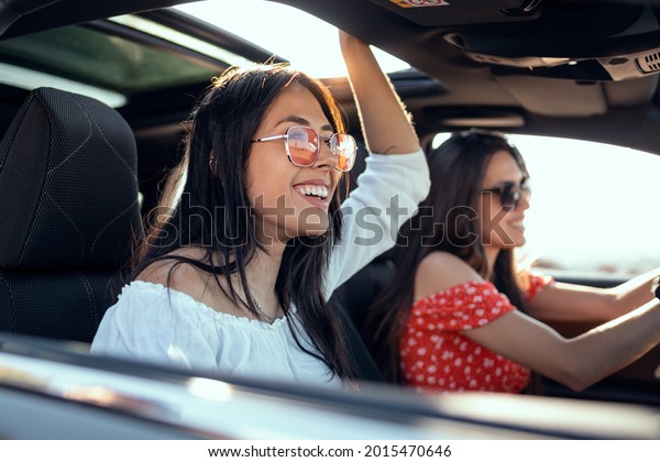 Shot of pretty young women singing\
while driving a car on road trip on beautiful summer\
day.