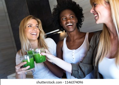 Shot Of Pretty Young Women Toasting With Detox Green Juice And Smiling At Home.