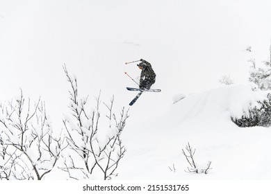 Shot of a professional freeride skier jump in the air over a snow-covered mountain slope. Freeride skiing concept