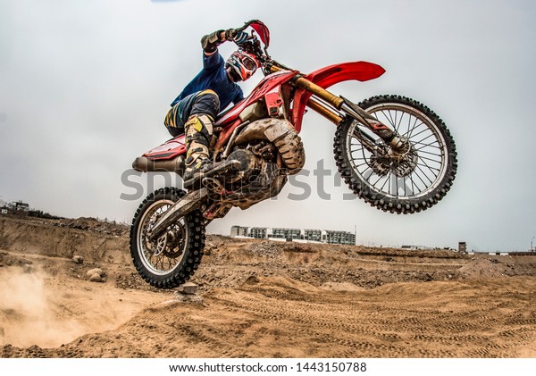 Shot of the professional
motocross rider on his motorcycle on the extreme terrain track.
Biker flying on a motocross motorcycle. Construction background and
sky.