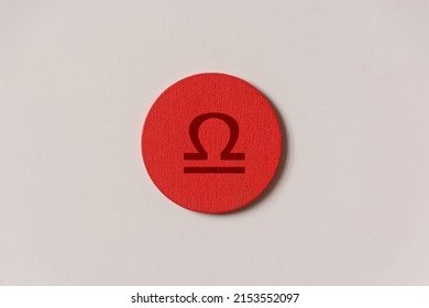 shot of a red wooden circle on a white background with a zodiac sign engraved on it, specifically the Libra sign